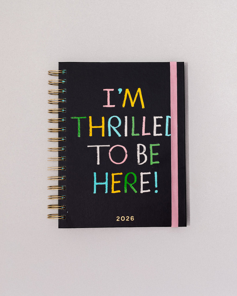 black 12-month planner with colorful 'i'm thrilled to be here' and pink elastic closure