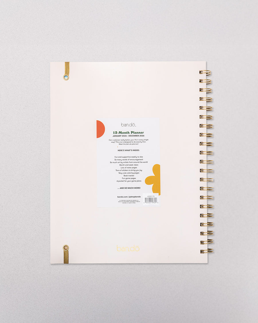 back view of cream large annual soft cover 12-month planner with colorful block lettered 'a work of art' typography with gold elastic closure