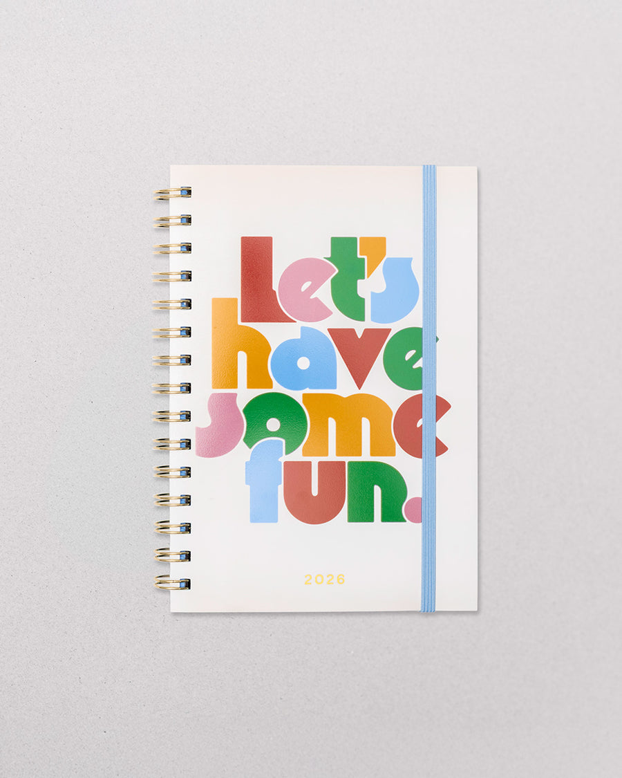 cream medium annual soft cover 12-month planner with colorful block lettered 'let's have some fun.' typography with light blue elastic closure