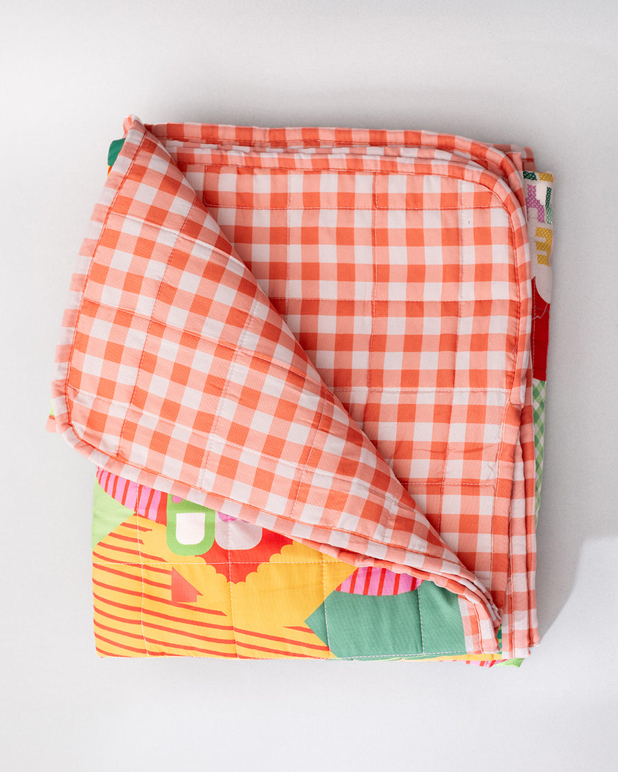 orange and cream gingham back side of quilted blanket with colorful ill and house print with 'house has my favorite places and faces' typography in the center