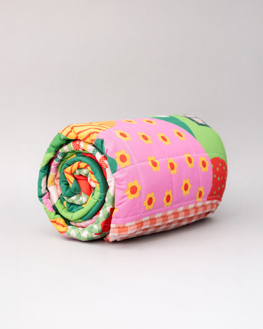 rolled quilted blanket with colorful ill and house print with 'house has my favorite places and faces' typography in the center