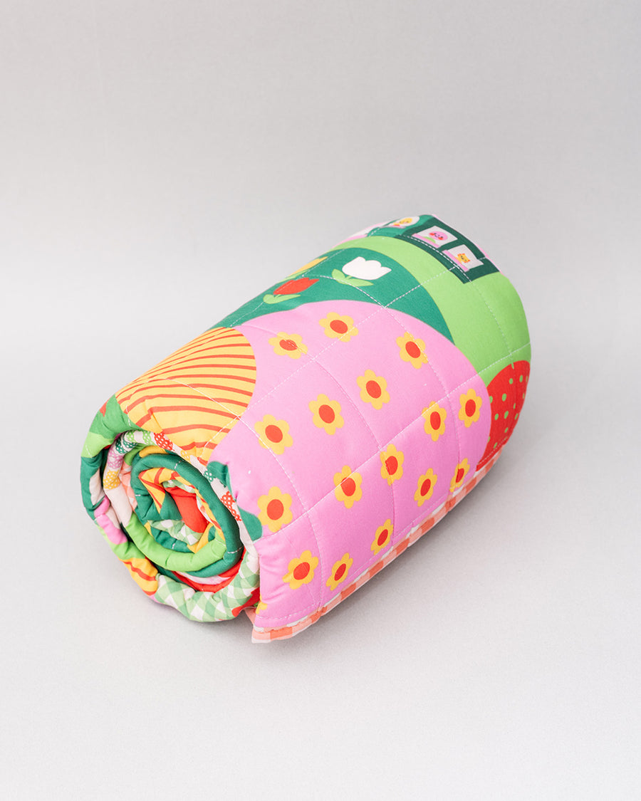 side view of rolled quilted blanket with colorful ill and house print with 'house has my favorite places and faces' typography in the center