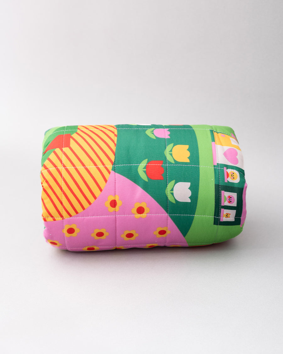 rolled quilted blanket with colorful ill and house print with 'house has my favorite places and faces' typography in the center