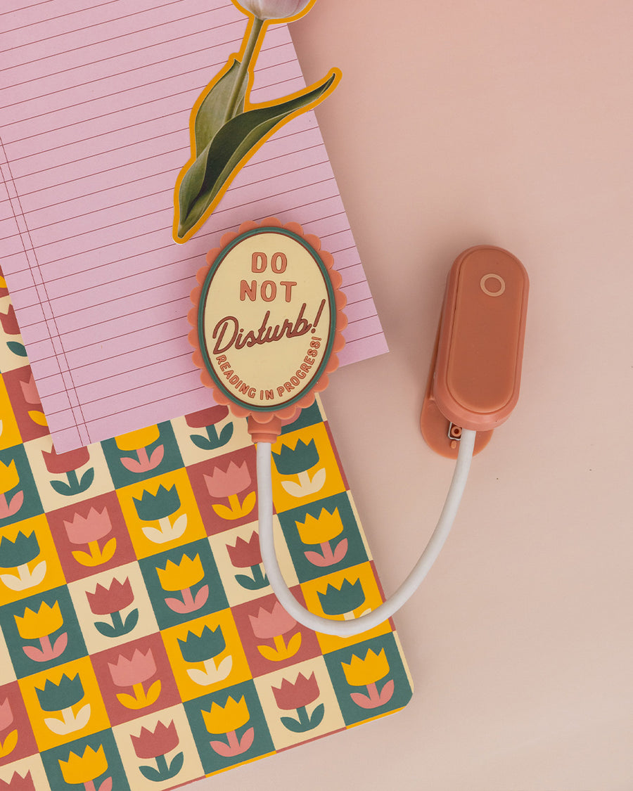 pink book light with pink and cream 'do not disturb! reading in progress!' on the top of the light on a pink background