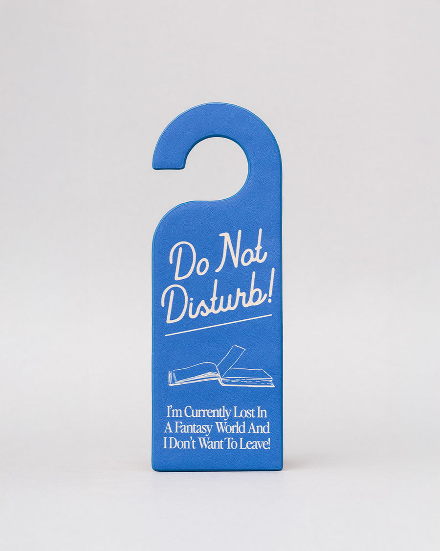 blue bookmark in the shape of a door hanger with white 'do not disturb!i'm currently lost in a fantasy world and i don't want to leave!' across the front