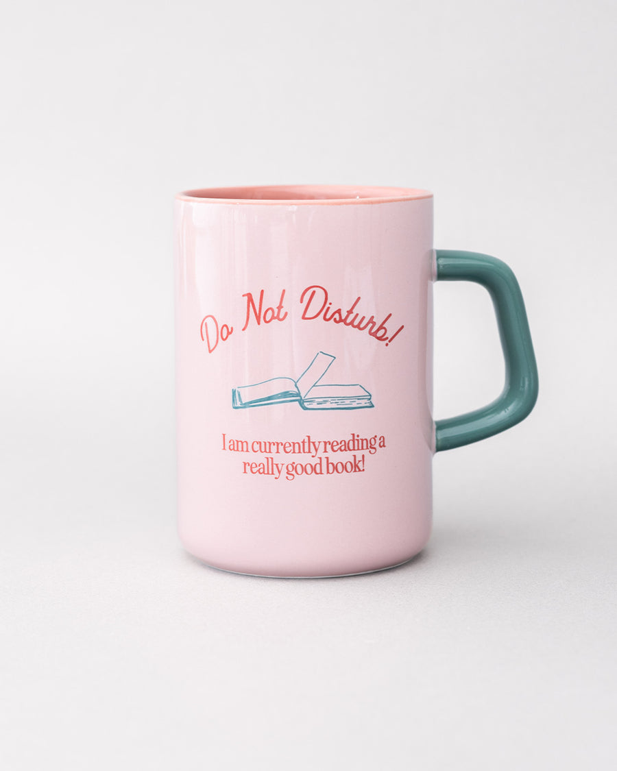 light pink ceramic mug with teal handle and 'do not disturb! i am currently reading a really good book!' typography on both sides