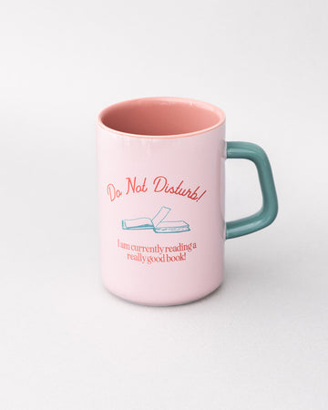 top view of light pink ceramic mug with teal handle and 'do not disturb! i am currently reading a really good book!' typography on both sides