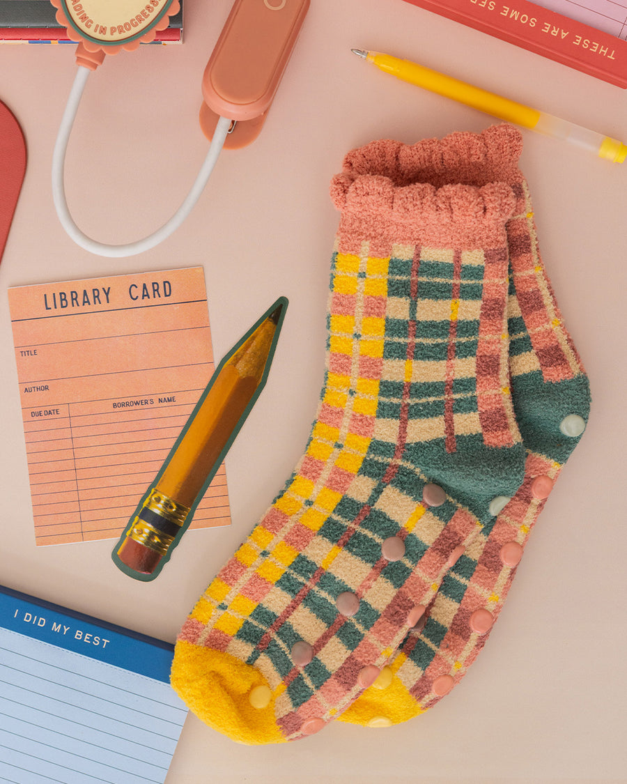 coral, teal, cream and yellow plaid chenille socks with coral ruffle top and cream grip bottoms on a pink background