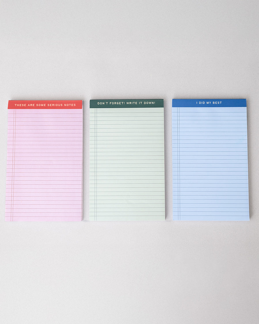 set of three ini legal pads: red/pink with 'these are some serious notes' on the top, green with 'don't forget! write it down!' and blue with 'i did my best' laid flat on a table