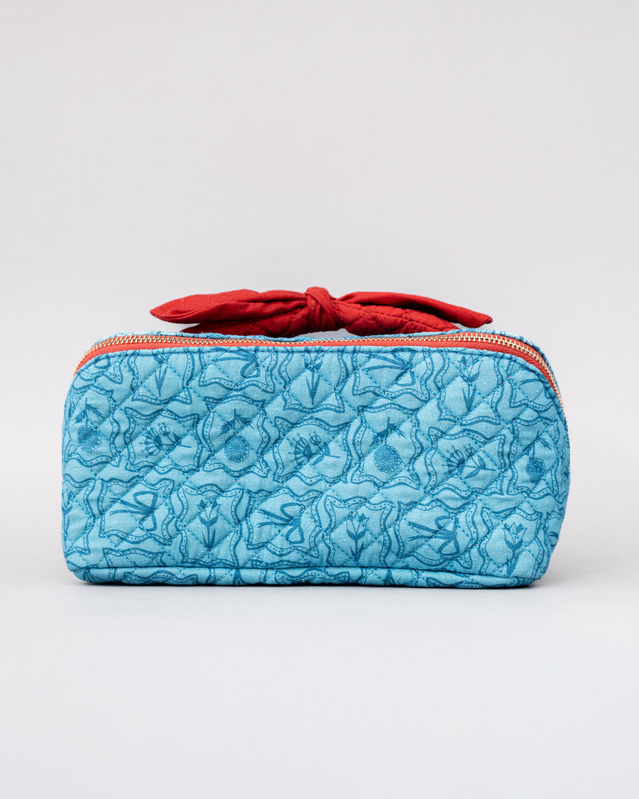 front view of blue quilted zipper makeup bag with red bow handle and all blue floral and bow print