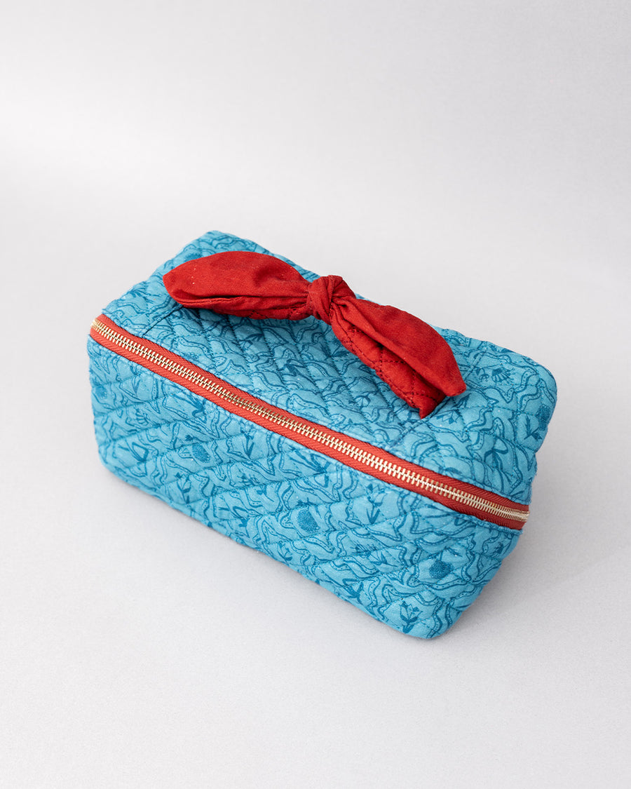 side view of blue quilted zipper makeup bag with red bow handle and all blue floral and bow print