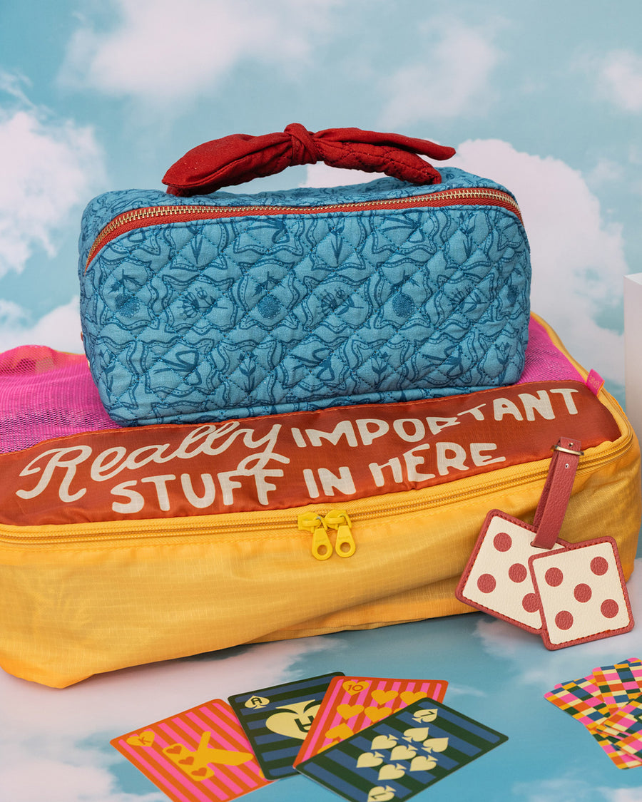 blue quilted zipper makeup bag with red bow handle and all blue floral and bow print on a colorful packing cube