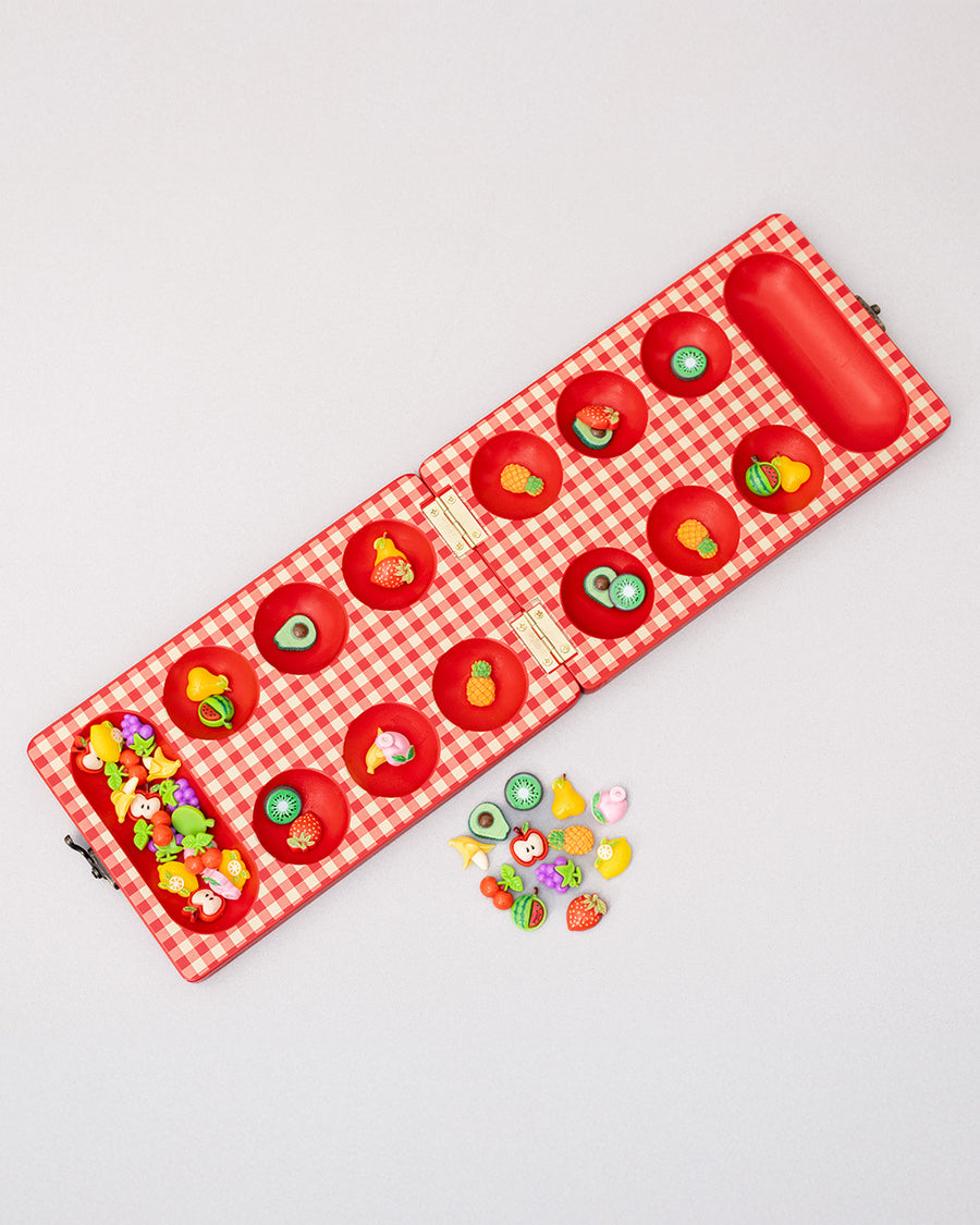 top view of red and cream gingham mancala board with colorful fruit game pieces