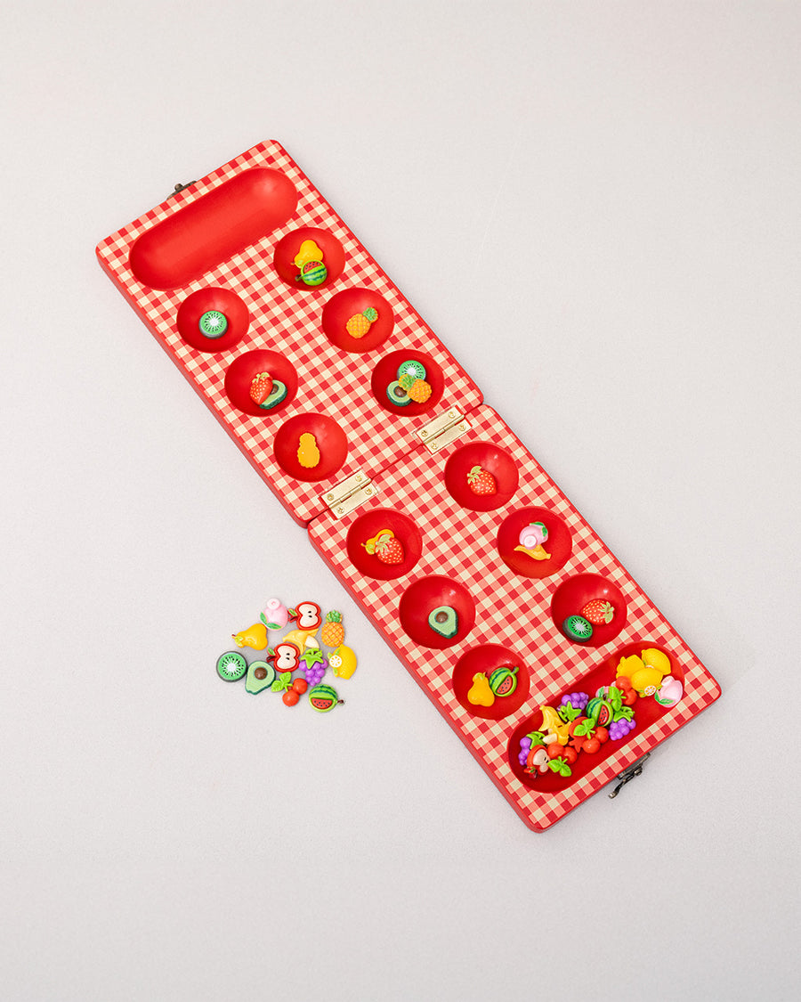 top view of red and cream gingham mancala board with colorful fruit game pieces