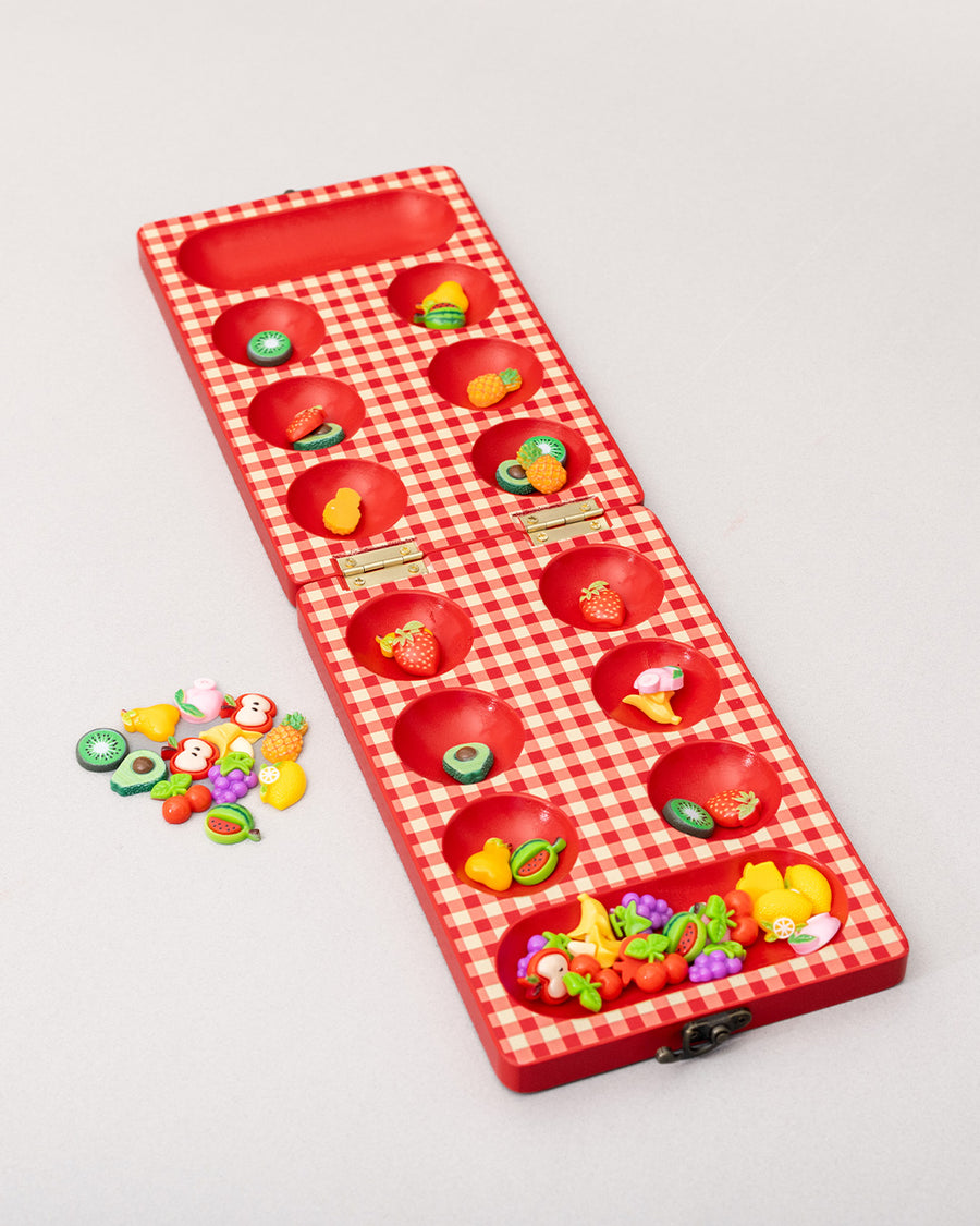 Wooden Mancala board game with colorful fruit-shaped pieces arranged across a printed board.