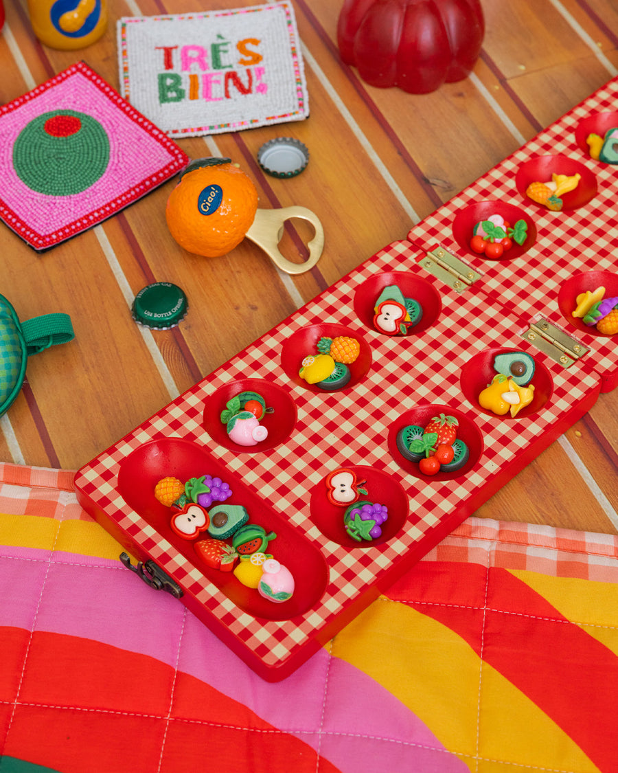 up close of red and cream gingham mancala board with colorful fruit game pieces on a table