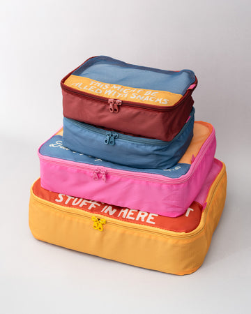 Set of four colorful packing cubes with different printed phrases, shown stacked together.