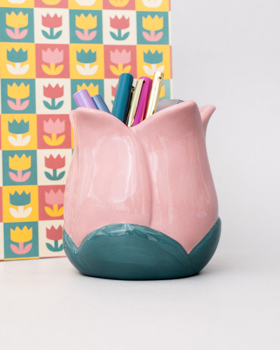 light pink tulip shaped pencil holder with pens inside and in front of a notebook
