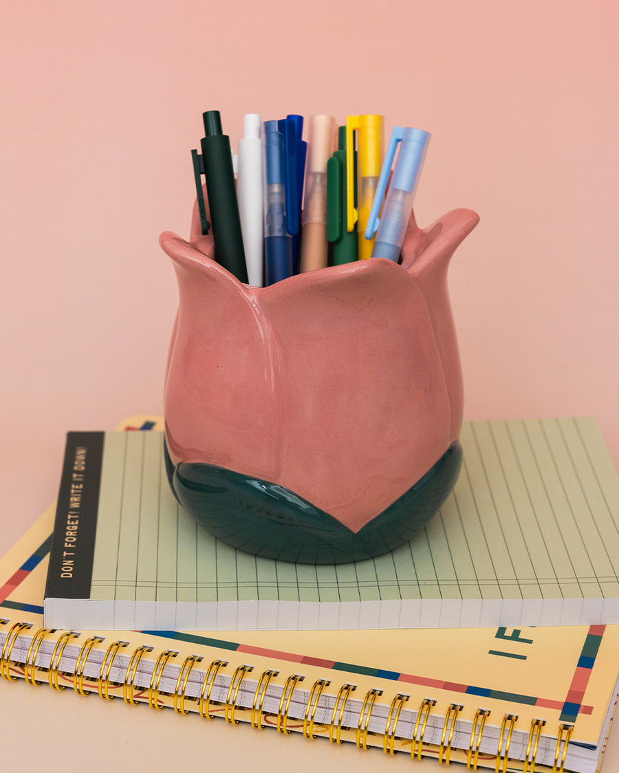 light pink tulip shaped pencil holder with pens inside on a stack of notebooks