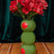 three green olives stacked vase on a green velvet background and has red flowers in it