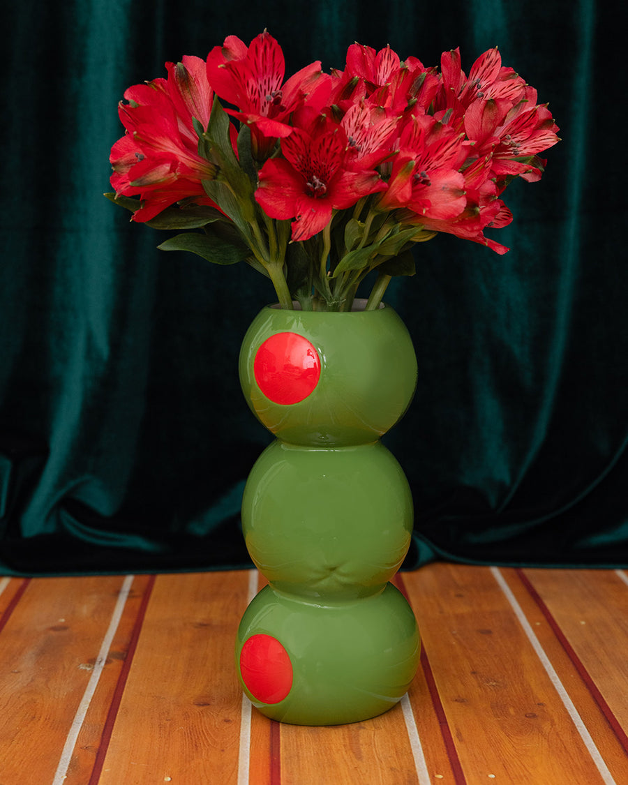 three green olives stacked vase on a green velvet background and has red flowers in it