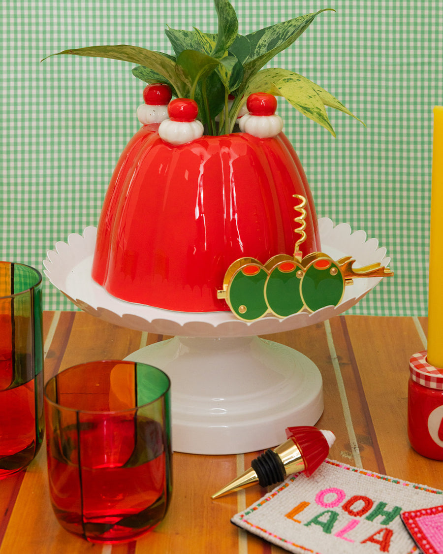 red jello mold vase/planter with a green plant inside on a stand surrounded by colorful kitchen items