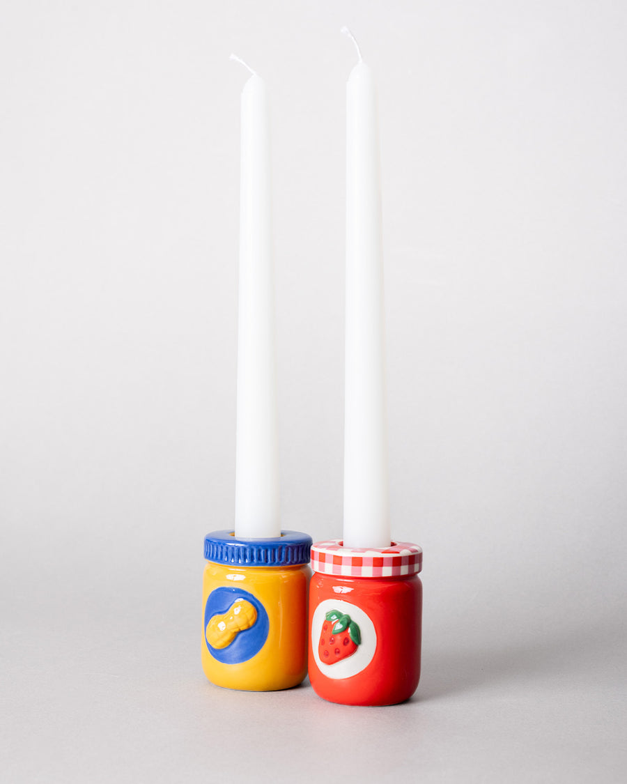side view of set of a peanut butter jar and jelly jar candle holders with white taper candles inside
