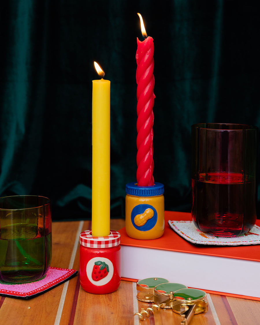 set of a peanut butter jar and jelly jar candle holders with colorful taper candles inside and surrounded by colorful kitchen items