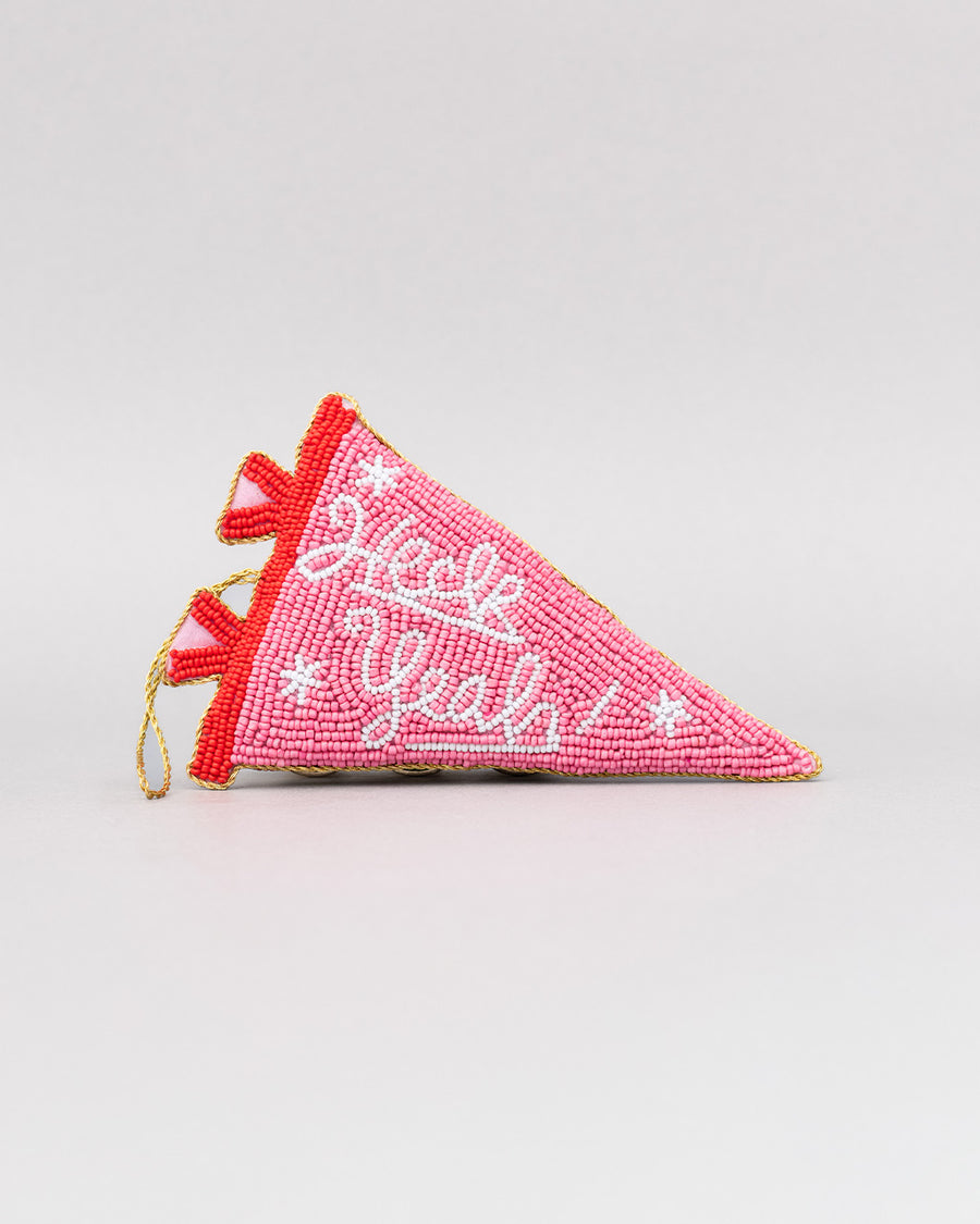 pink beaded pennant ornament with white cursive 'heck yeah!' across the front