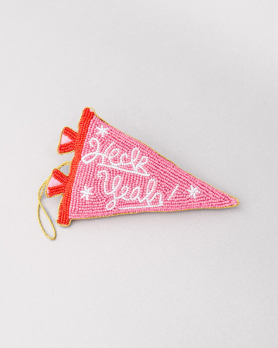 pink beaded pennant ornament with white cursive 'heck yeah!' across the front