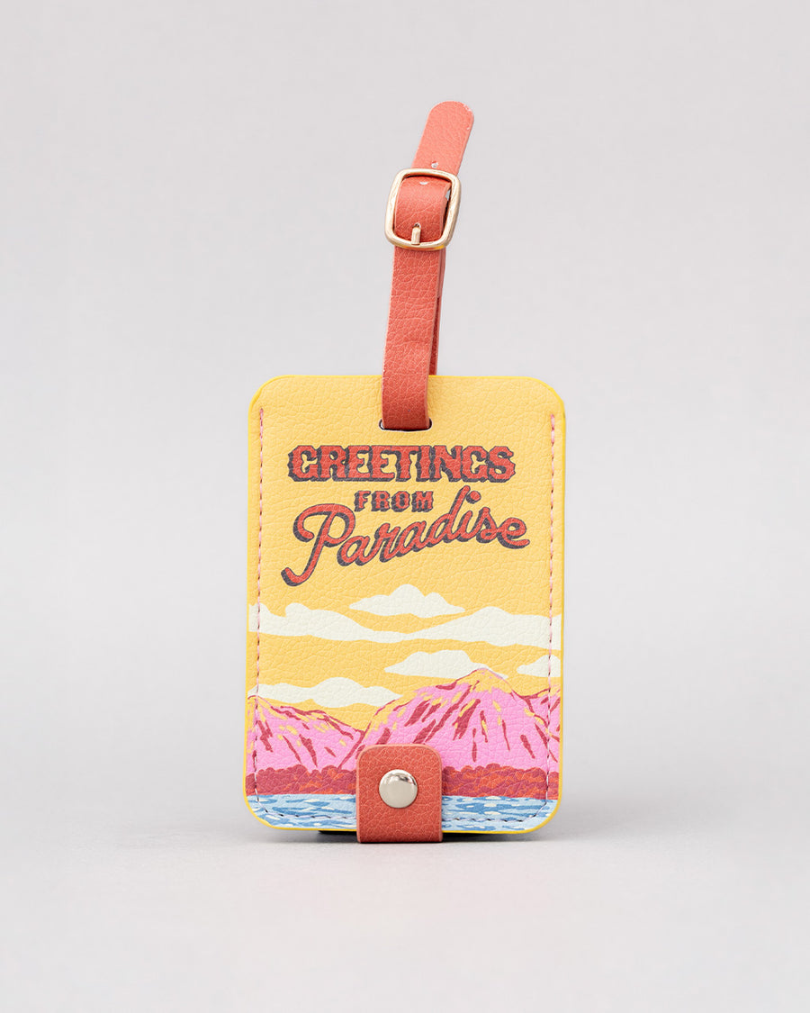 luggage tag with colorful mountain scene and red 'greetings from paradise' across the front
