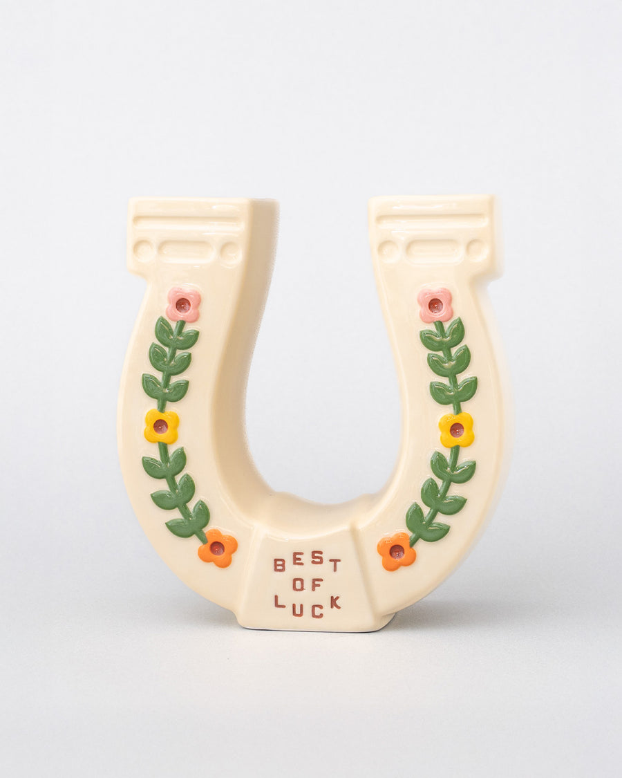 front view of cream horseshoe ceramic vase with colorful flower trim and 'best of luck' stamp in the center