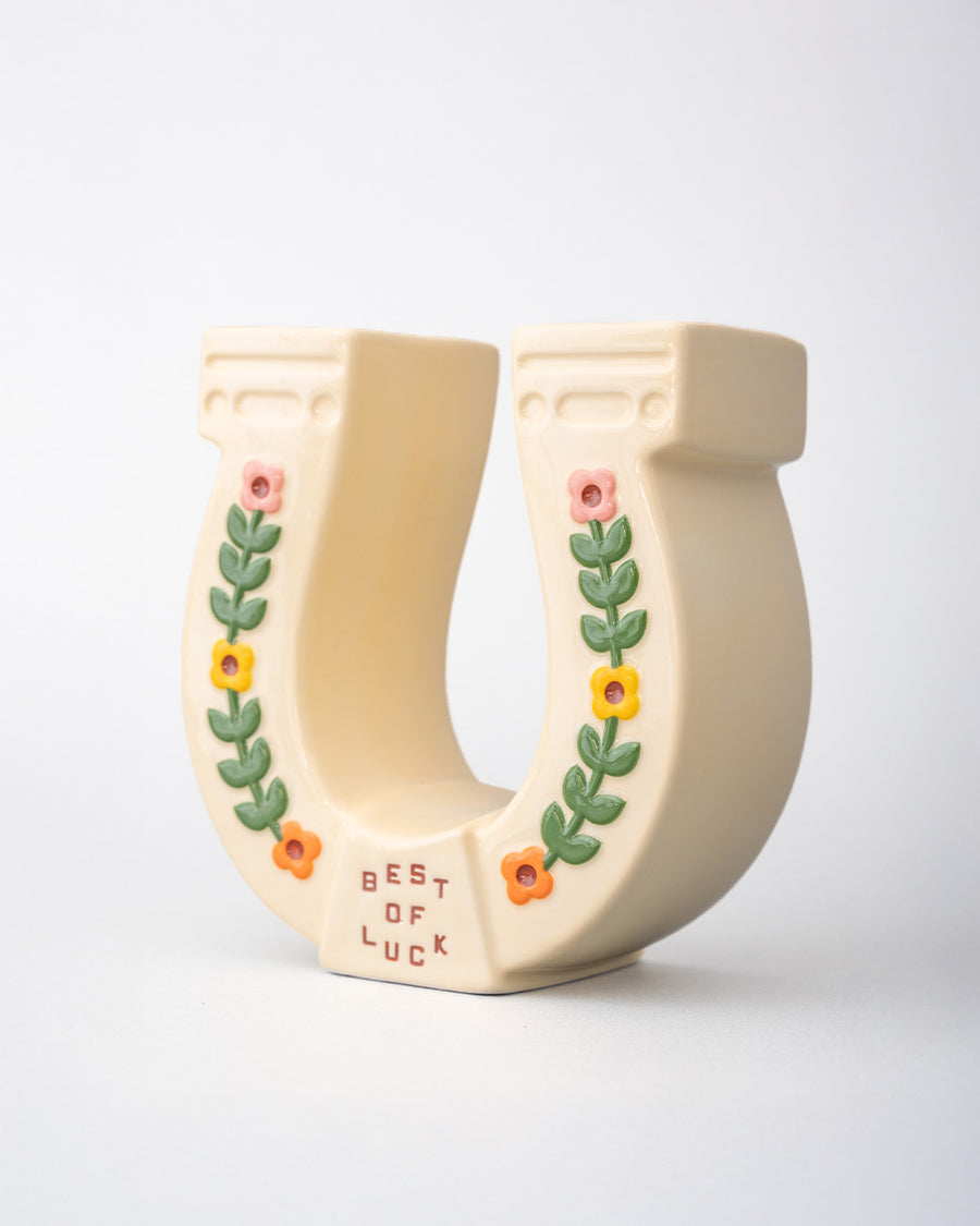 side view of cream horseshoe ceramic vase with colorful flower trim and 'best of luck' stamp in the center