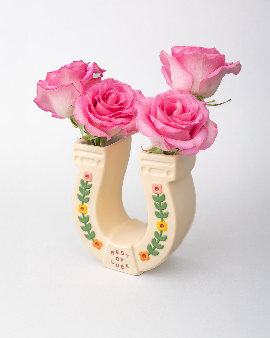 sideview of cream horseshoe ceramic vase with colorful flower trim and 'best of luck' stamp in the center with roses inside