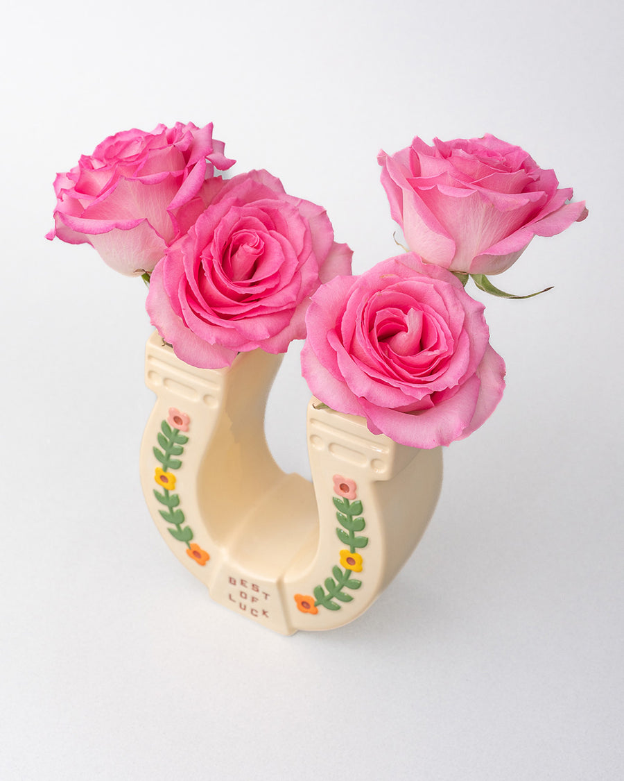 top view of cream horseshoe ceramic vase with colorful flower trim and 'best of luck' stamp in the center with pink roses inside