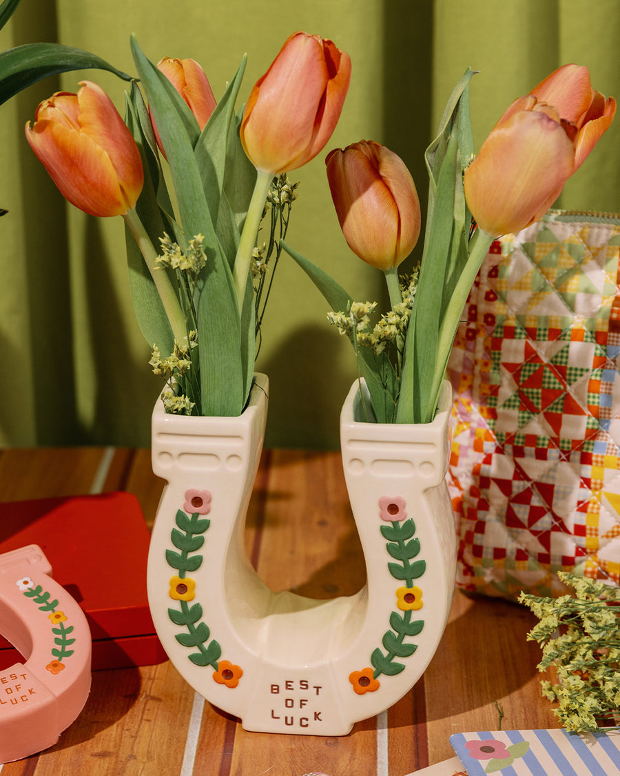 cream horseshoe ceramic vase with colorful flower trim and 'best of luck' stamp in the center with pink roses inside