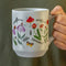 model holding white ceramic coffee mug with colorful wildflower botanical print