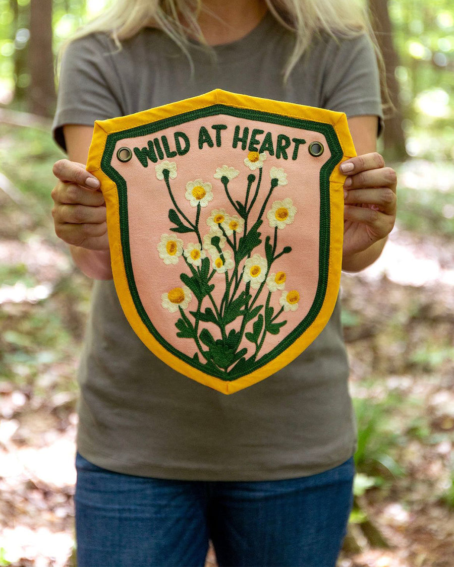 model holding yellow, green and pink embroidered banner with wildflowers and 'wild at heart' across the top