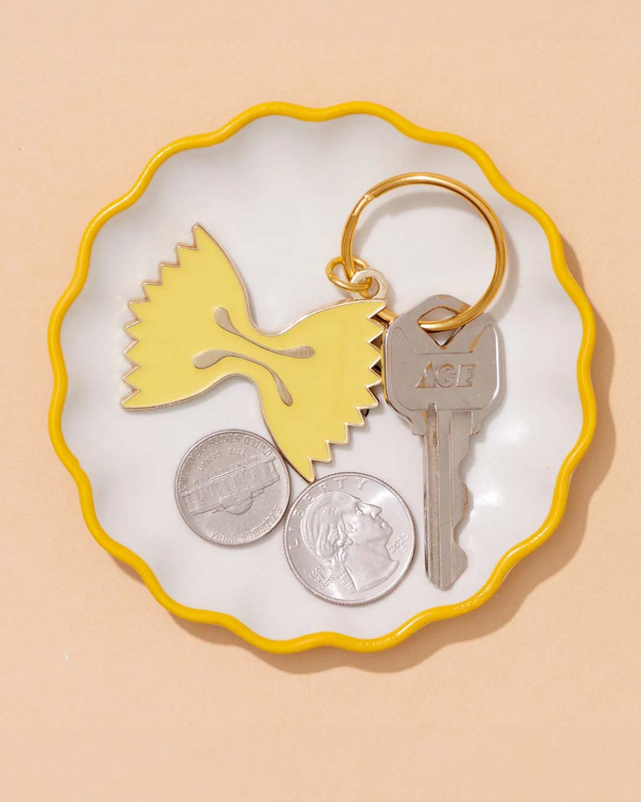 yellow enamel bowtie pasta keychain on tray with coins and key