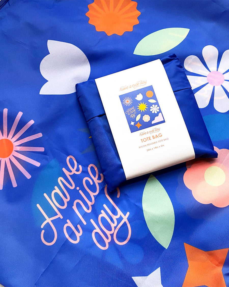 up close of packaged royal blue reusable bag with abstract floral print and 'have a nice day' on the front