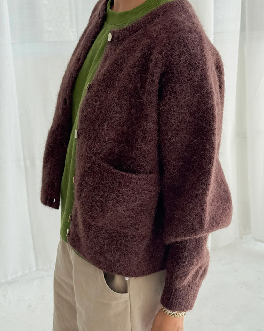 sideview of model wearing dark brown oversized cardigan with shell buttons and two front patch pockets 