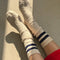 model wearing heather oatmeal crew socks with double navy stripes at the top with no shoes on