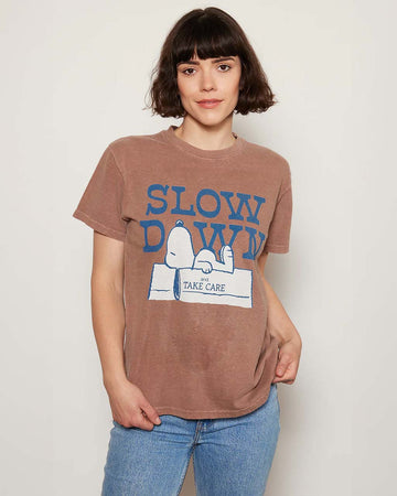 model wearing brown relaxed tee with snoopy graphic 'slow down and take care' typography