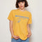 model wearing yellow relaxed tee with 'woodstock est 1969' blue typography and peanuts woodstock graphic