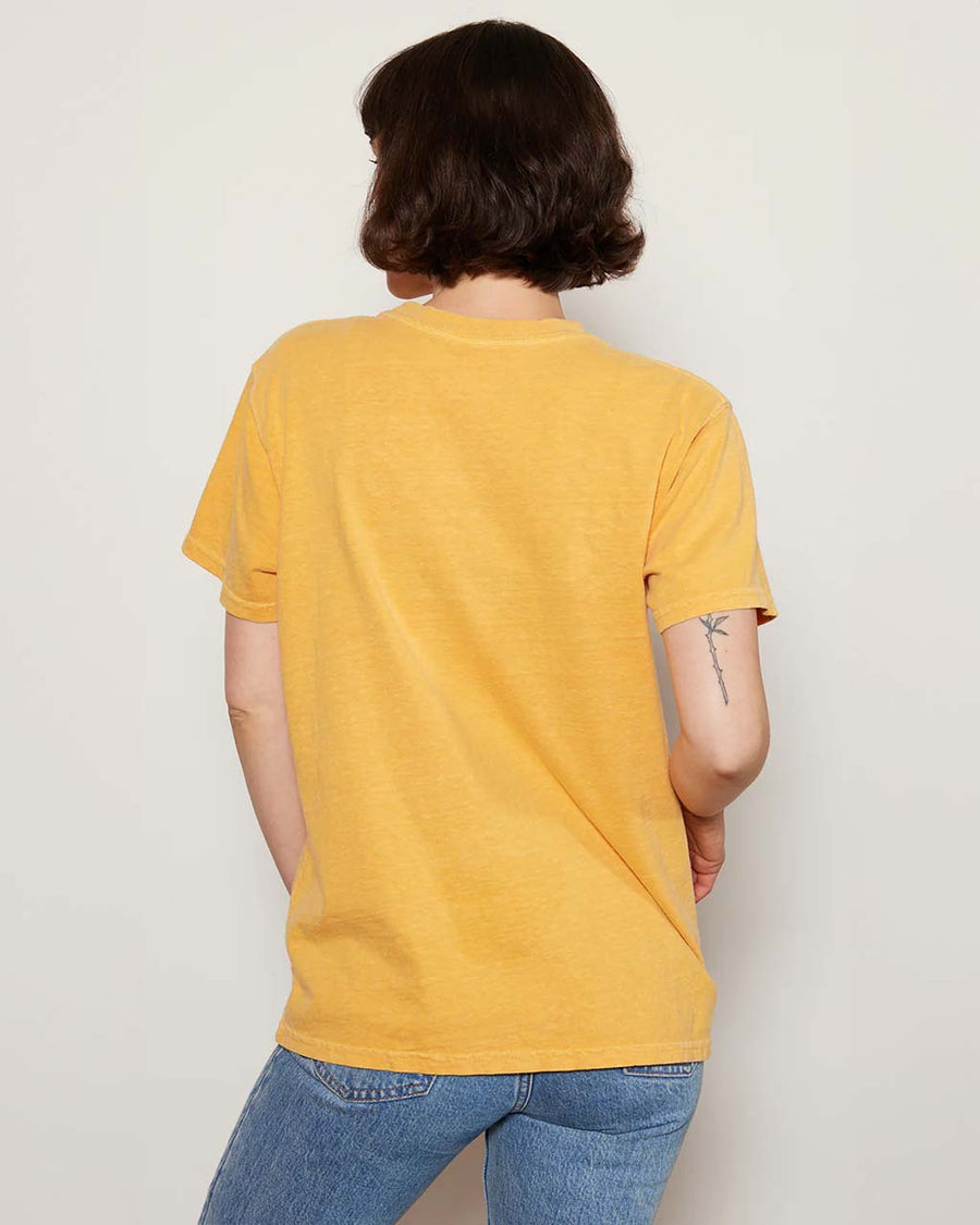 back view of model wearing yellow relaxed tee with 'woodstock est 1969' blue typography and peanuts woodstock graphic