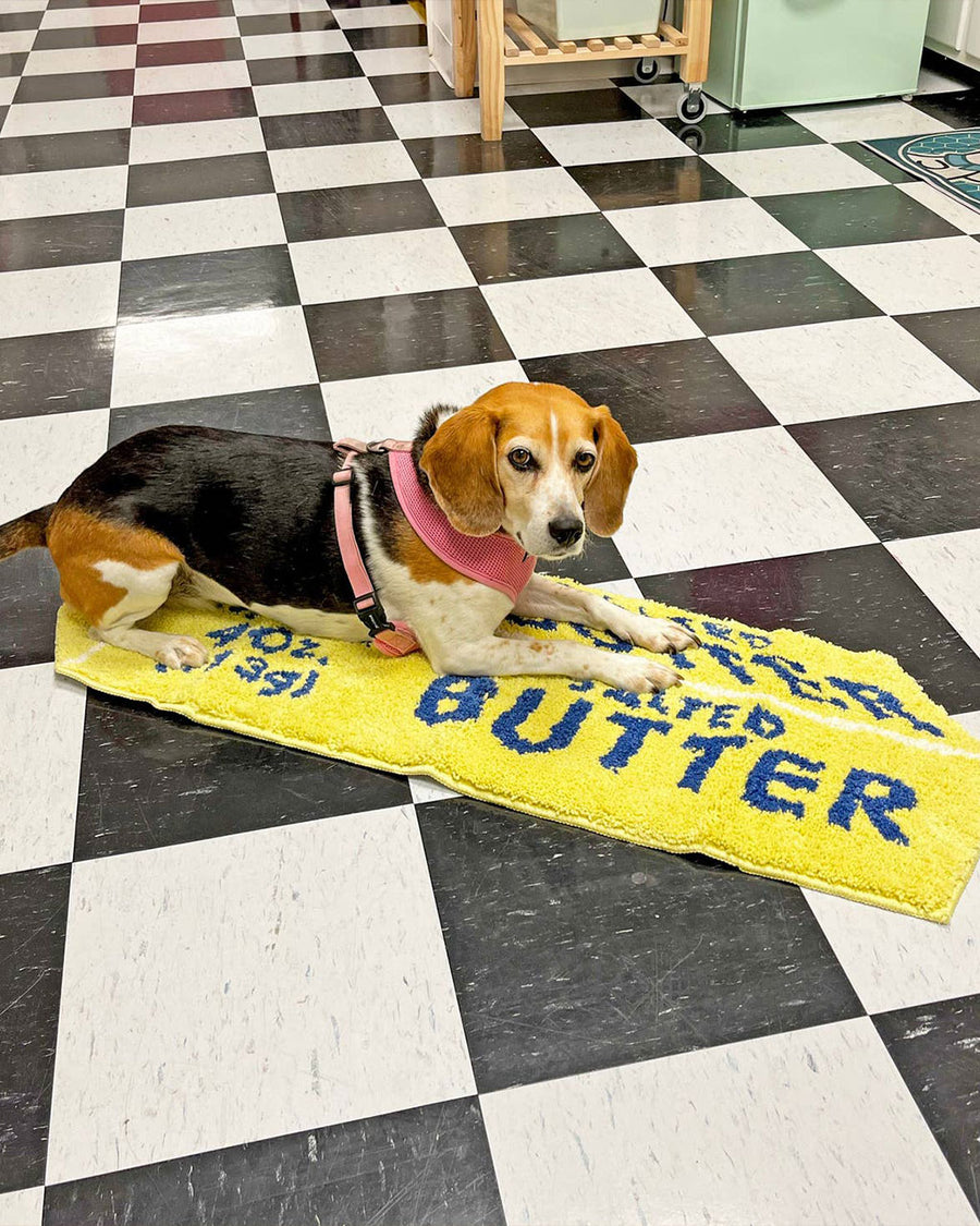 stick of salted butter shaped throw rug with dog laying on it