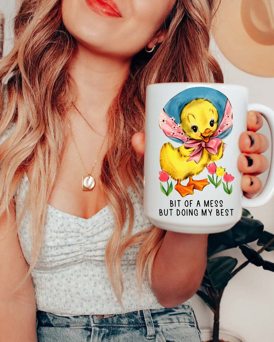 model holding 15 oz. white mug with yellow duck and says 'bit of a mess, but doing my best'