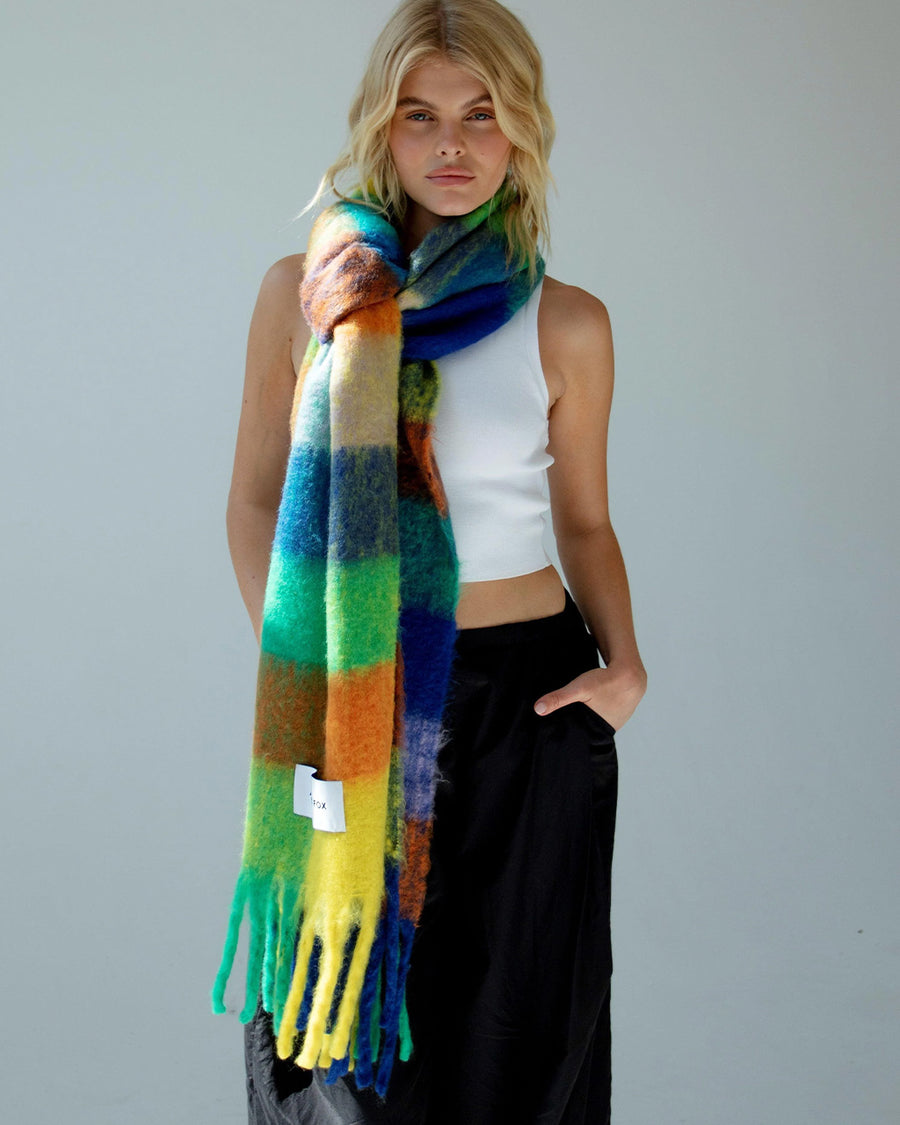 model with tied multicolored oversized checkered scarf with fringe around their neck