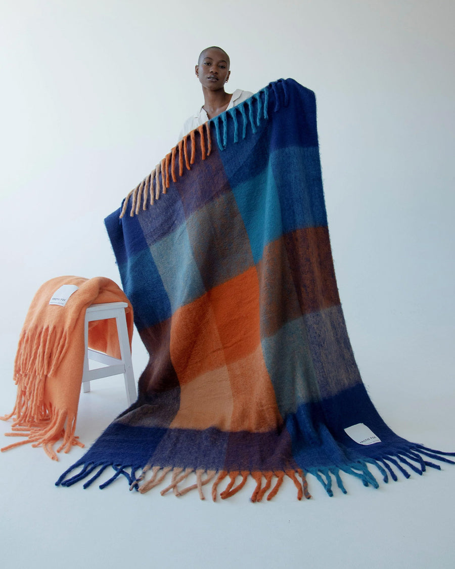 model holding up navy, light blue, orange and yellow checkered throw blanket with fringe