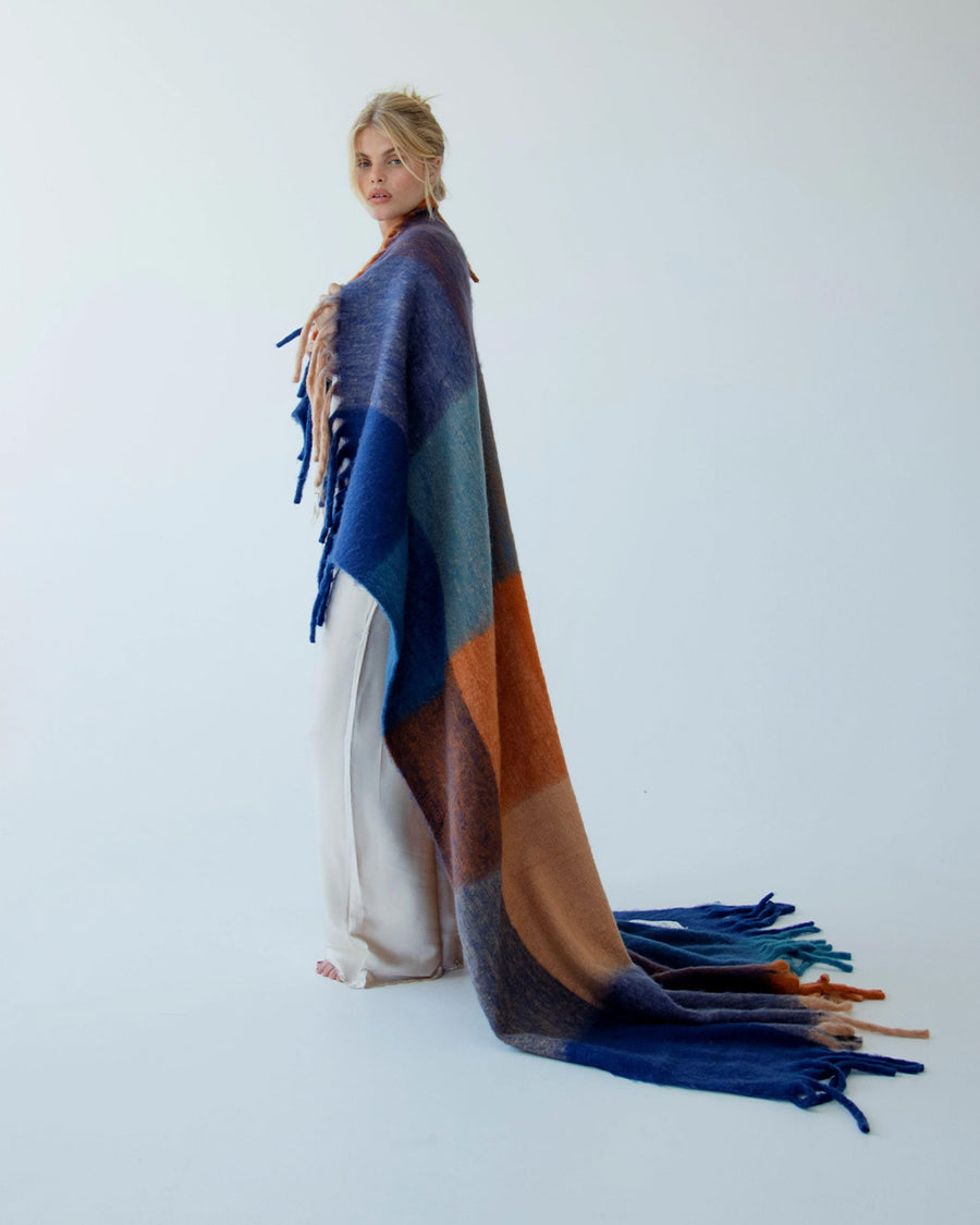 model wrapped with navy, light blue, orange and yellow checkered throw blanket with fringe